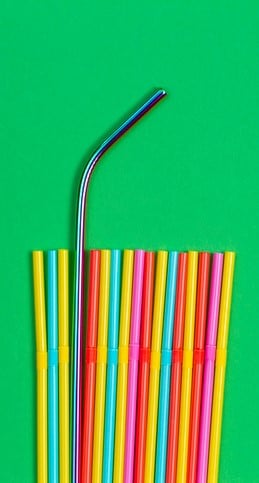 Las pajitas de metal son pajitas reutilizables ideales como alternativa a las de plástico de un solo uso. En la foto, una pajita de metal sobresale entre un grupo de pajitas de plástico de colores.