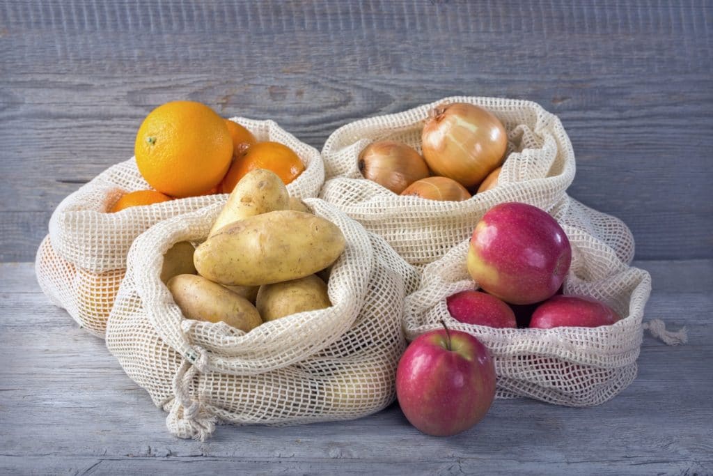 4 bolsas de malla para frutas y verduras que contienen manzanas, cebollas, naranjas y patatas. ¡Pásate ya a las bolsas reutilizables y deja atrás los plásticos de un solo uso!