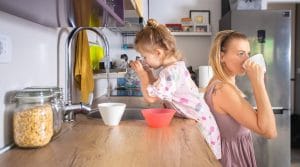 Agua del grifo y coronavirus: en esta imagen aparece una niña llenando un vaso de agua en el grifo de la cocina, y a su espalda, su madre bebiendo de una taza. | Vive sin plástico